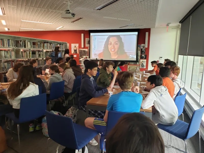 Students watch screen from tables in classroom