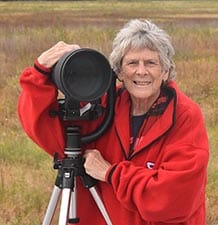 Marian Brickner poses in nature with her large wildlife camera