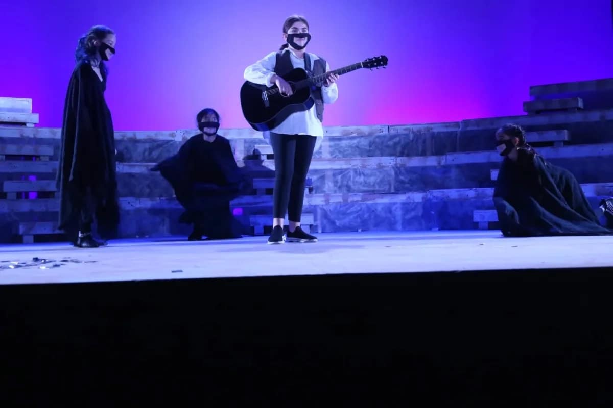 Student plays guitar on stage during theater performance