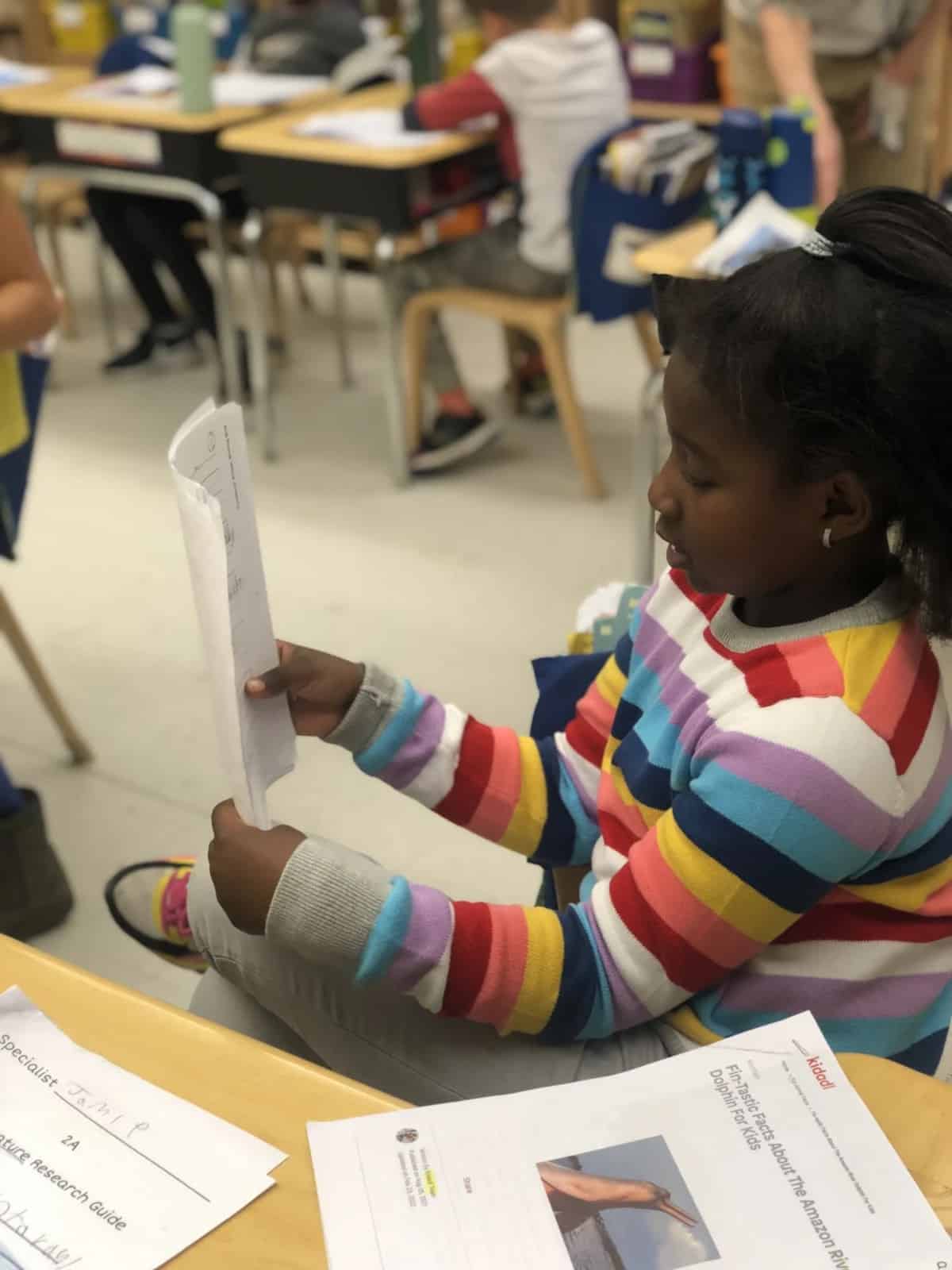 Student reads from her project while sitting at desk