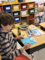 Student sits at desk and works on painting