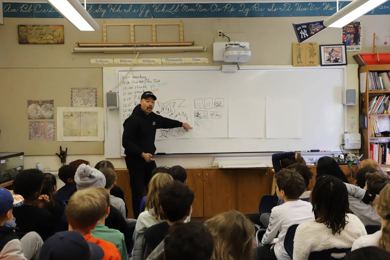 Craft instructs young students while pointing at drawing on whiteboard