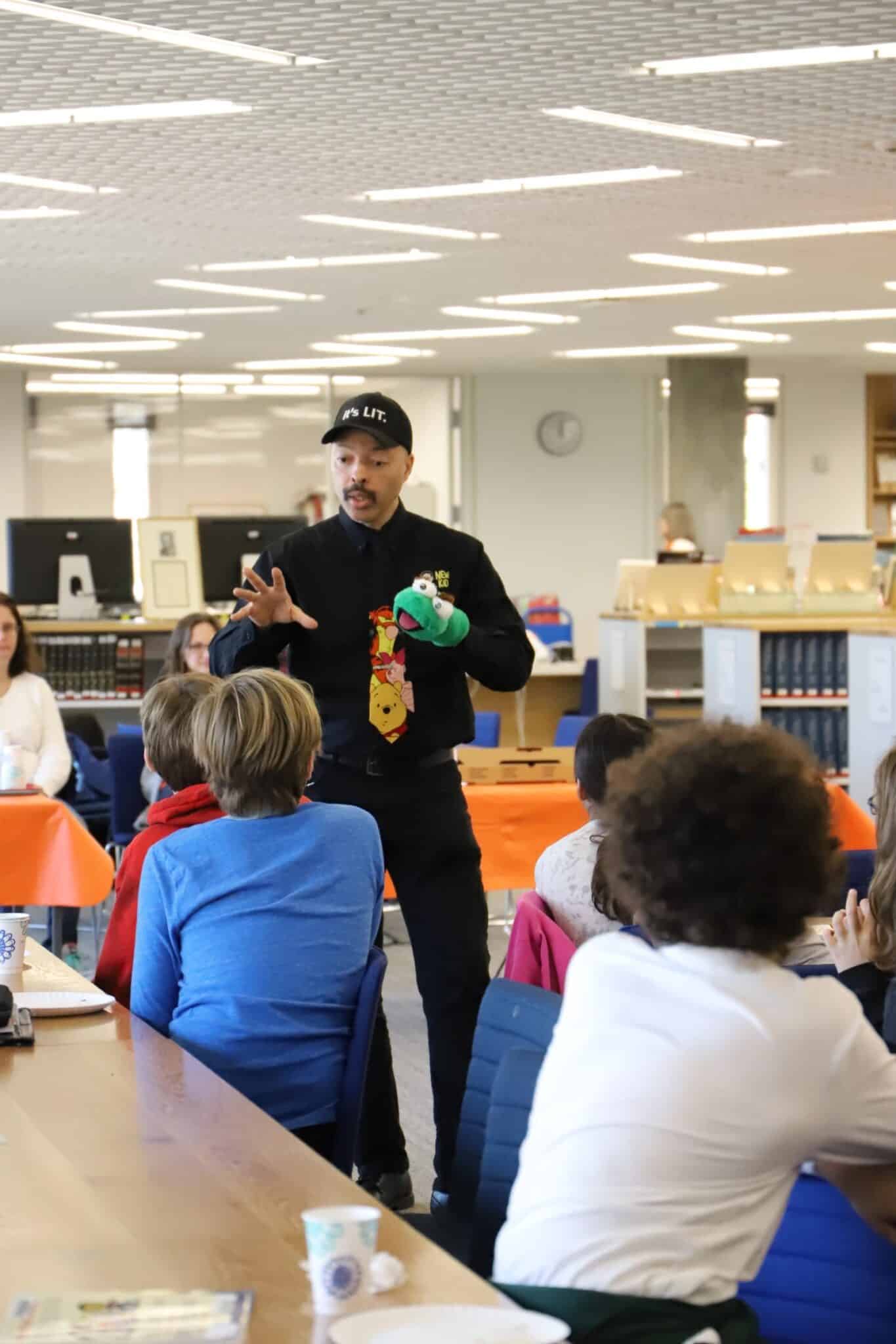 Craft speaks to students using sock puppet in library