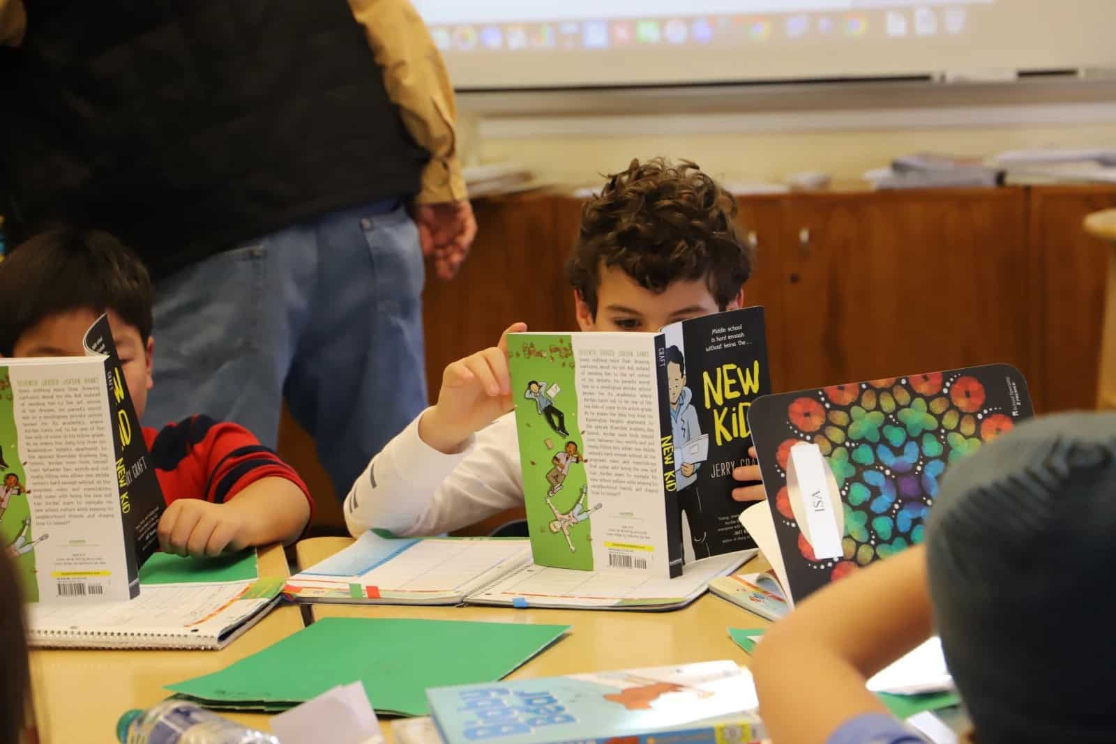 Student reads "New Kid" while sitting at his desk