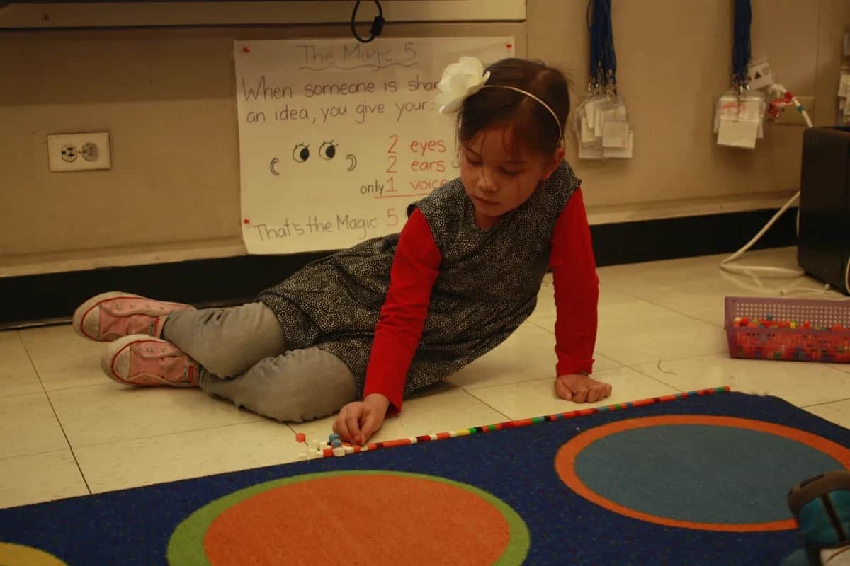 Student lines cubes along carpet while sitting on floor