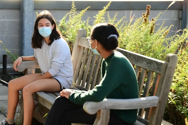 Two students speak while sitting on bench outdoors