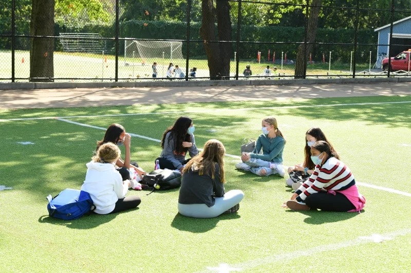 Students sit in circle on field outdoors