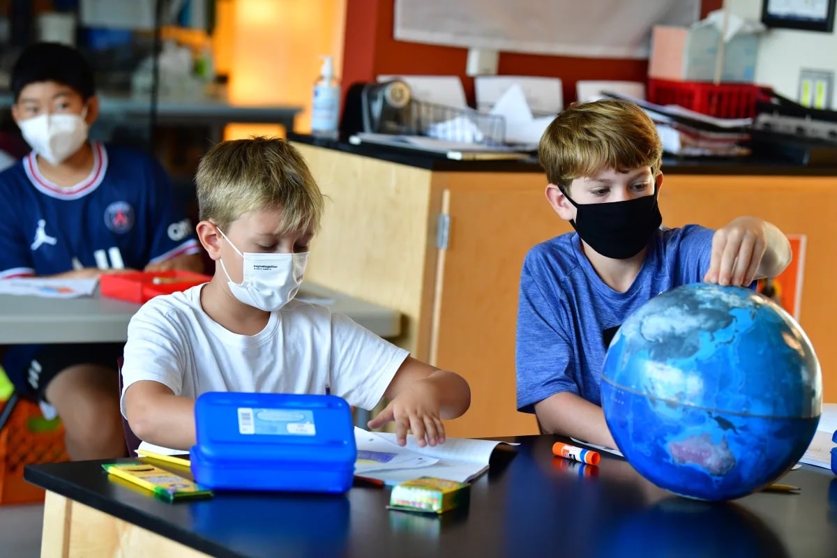 Two students inspect a globe while sitting at desk