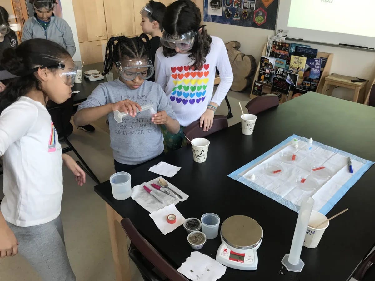 Students, wearing goggles, conduct an experiment